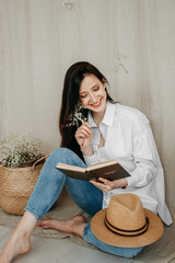 Photo of a beautiful young girl with long hair sitting on the floor and reading an open book. The...