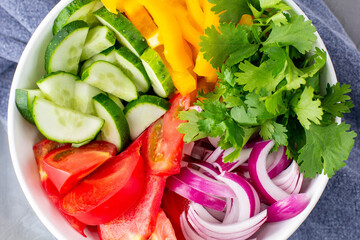 Plate of rainbow salad with different vegetables and herbs in white bowl on grey stone background