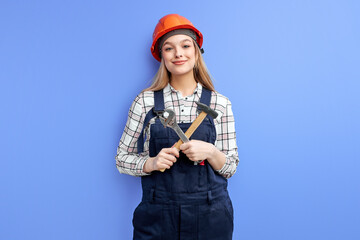 female constructor in orange helmet standing with tools against blue wall