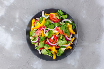 Plate of rainbow salad with different vegetables and herbs on black plate on grey stone background