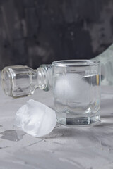 a shot glass with ice ... ice cubes next to her ... behind the glass is the neck of a bottle with a...