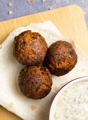 Three balls of falafel on a piece of pita bread on a wooden board, vegan sauce with herbs in the corner