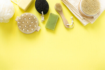 Products and items for bathroom. Massage brushes, soap, pumice stone and towel on yellow background, copyspace
