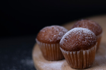 three muffins covered in powdered sugar on wooden stand isolated on black dark background. sweet bakery