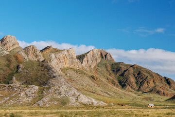 A mountain of unusual texture in the steppes of Tuva, a stone ridge against the background of the sky with clouds
house at the foot of the mountain