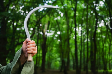 man's hand with a sickle in dark forest