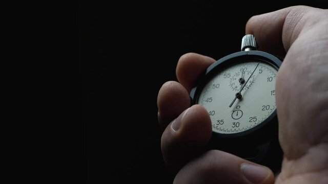 Black analogue stopwatch in hand on black background. Time start with old chronometer. Man presses start button. Sport or business concept. Successful teamwork. Counts down time