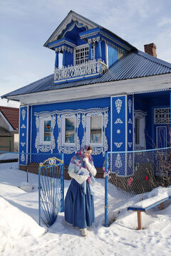 Russian girl in Pavlovo Posad shawl. Wooden rural house with carved windows in Purekh village, Nizhny Novgorod region, Russia. Snow winter. Russian folk style in architecture, architectural fashion