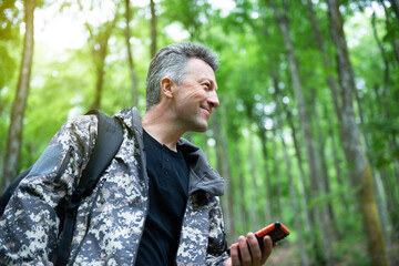 Mature man walking and hiking in mountain forest and using mobile phone. Male spring outdoor portrait.