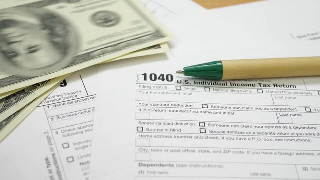 100 dollar bills on 1040 tax form. Green pen on table in office. U.S. individual income tax return. Tax payment concept. Filing taxes document. Count the money