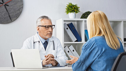 Obraz premium blonde woman talking to attentive doctor during appointment in clinic