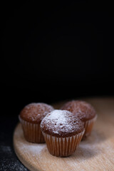 three muffins covered in powdered sugar on wooden stand isolated on black dark background. sweet bakery
