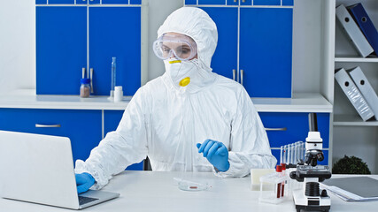 virologist in hazmat suit working on laptop in laboratory