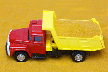 Toy dump truck delivering sand.   Sand background. Transportation of bulk materials