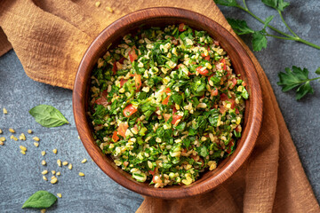 Traditional Arabic salad tabbouleh in a wooden bowl on a dark background top view. Arabic cuisine, vegan food. 