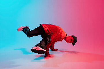 Beautiful sportive boy dancing hip-hop in stylish clothes on colorful gradient background at dance hall in neon light.