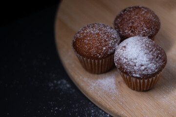 three muffins covered in powdered sugar on wooden stand isolated on black dark background. sweet bakery