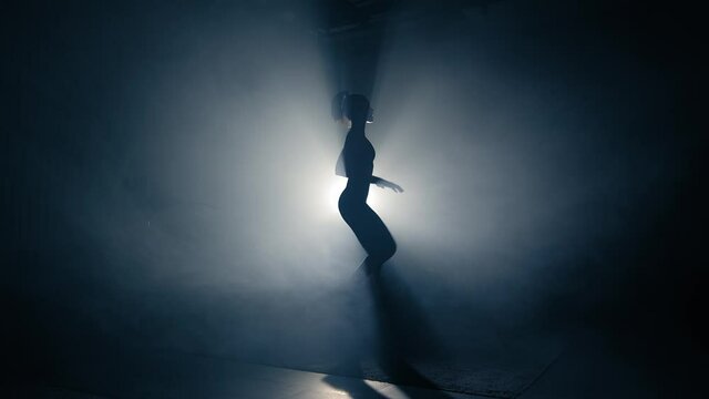 Fit woman training silhouette. Backlighted woman silhouette doing high knee exercises. Side view, slow motion
