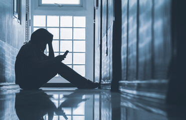Depressed woman sitting alone and looking smartphone with holding her head on corridor in front of...