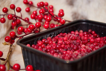 Frozen winter berries with ice in a bowl on the table branches and leaves food blurred background