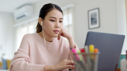 Candid young attractive asian female employee wear earphone listen to digital online course...