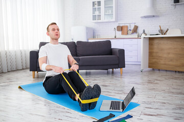 Online training. Young man doing exercise with fitness rubber bands with online tutorial at home,...