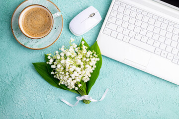 Home office desk table with coffee cup, bouquet of spring flowers lily of the valley. Workplace with laptop and coffee on green background. Blogging, freelance, florist concept. Top view, flat lay