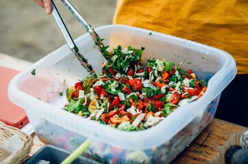 kitchener is using tongs to take the raw salad, vegan healthy salad bowl closeup, vegetables