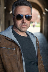 Urban outdoor portrait of a handsome mature man wearing brown jacket with sunglasses, street style...