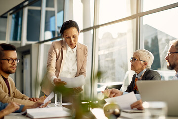 Asian female business leader analyses report data while meeting with business team in the office.