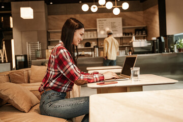 side view of happy freelancer using laptop while sitting on couch in cafe