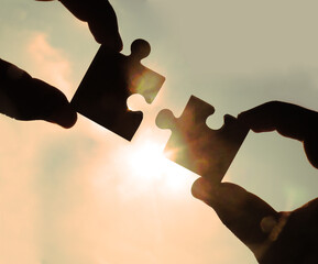 two hands trying to connect couple puzzle piece with sunset background. Jigsaw alone wooden puzzle...