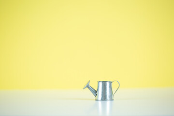 small metal watering can, on a yellow background with a copy of the space