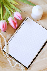checkered empty notebook with pink tulips, white candle and pearls on fabric background
