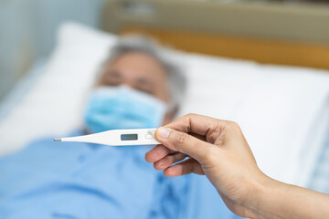 Doctor holding digital thermometer to measures asian senior or elderly old lady woman patient wearing a face mask have a fever in hospital, healthy strong medical concept.