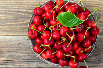 Ripe sweet cherries with green leaves in a metal plate on wooden background