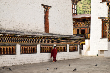 A monk walking next to the prayer wheels in the inner courtyard in Tashichho Dzong. Thimphu, Bhutan.