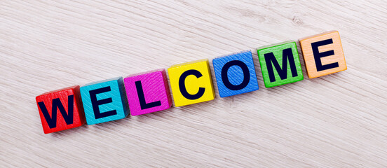 On a light wooden background on multi-colored bright wooden cubes the word WELCOME