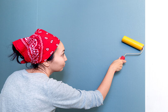 Happy woman smoothes air and glue bubbles on the wallpaper with a roller. An experienced master applies various techniques to properly prepare the walls