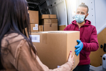 Young man courier with his van delivers a package to female recipient wearing gloves and face mask...