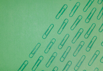 Green paper clips isolated on green background, close up, copy space. Top view. Back to school, college, education concept