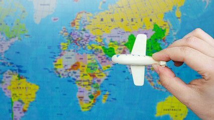Fototapeta na wymiar A small white toy airplane in a woman's hand on the background of a world map. Travel concept