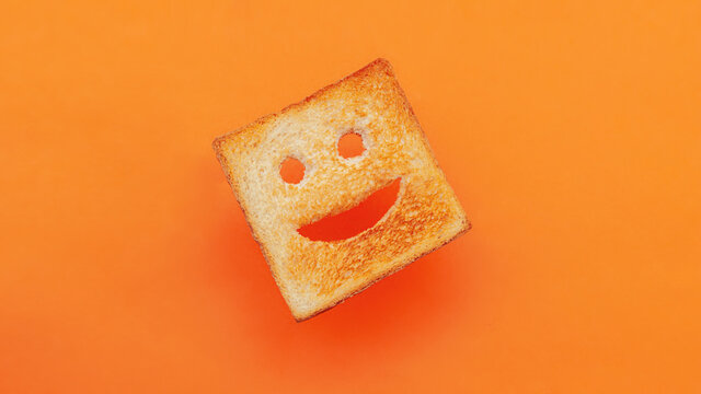 Funny smiling bread toast on a orange background. Good mood, positive emotions, joy, happiness, good morning, delicious breakfast for kids