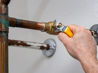 Plumber turning water shut off valve. Copper plumbing pipe with brass water supply valve and yellow...