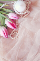 romantic background with pink tulips, pearls and white candle on tulle fabric with space for text