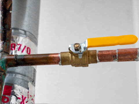Water shut off valve. Copper plumbing pipe with brass water supply valve and yellow stopcock handle.