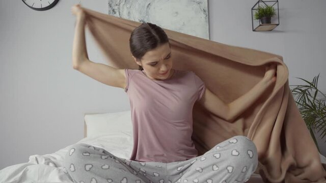 young woman feeling cold and covering with blanket in bedroom