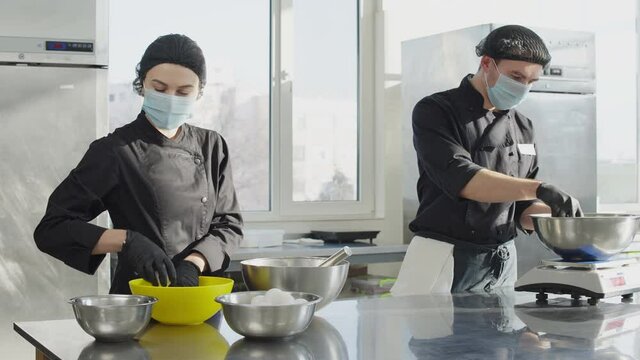 Portrait of young Caucasian male and female confectioners working in kitchen. Woman putting eggs in bowl and leaving as man gathering ingredients for sweet pastry. Food industry concept.