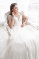 Fototapeta na wymiar Beautiful bride in a beautiful wedding dress poses on the background of a hotel room
