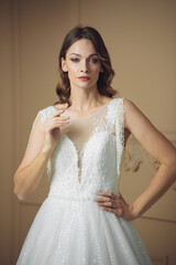 Beautiful bride in a beautiful wedding dress poses on the background of a hotel room